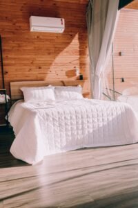 A stylish bedroom featuring a double bed with white bedding, wooden walls, and natural light.