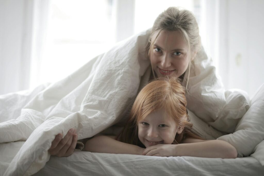 A joyful mother and daughter share a warm moment under a cozy blanket at home.