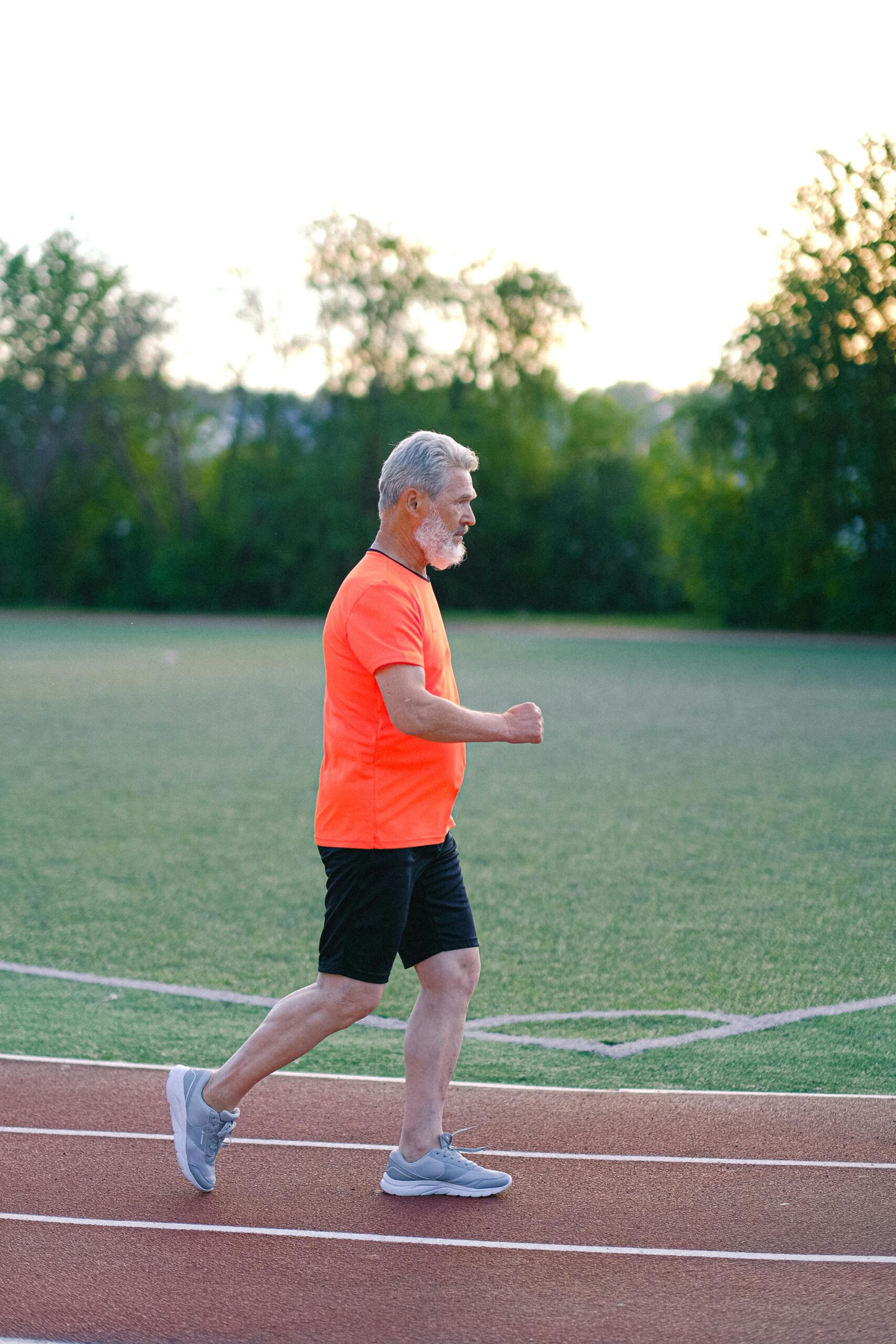 Side view of sporty senior male running on stadium track while preparing for marathon
