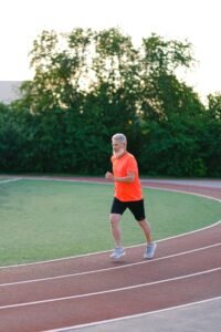 Full body of elderly male jogging in stadium surrounded with lush green bushes
