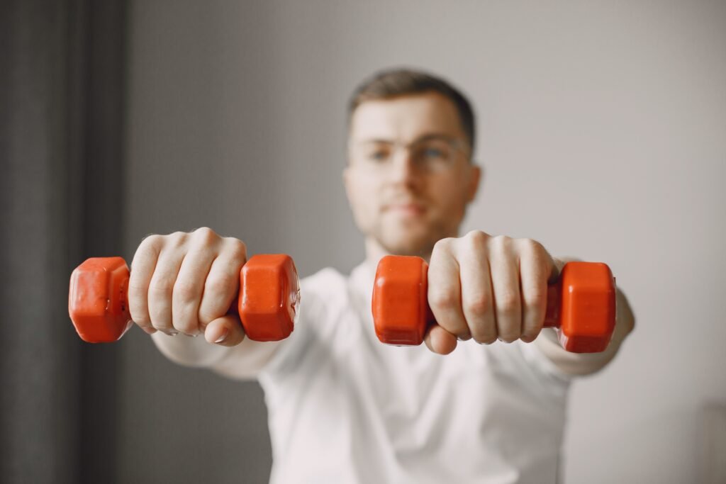 Focused adult male exercising with red dumbbells at home, promoting a healthy lifestyle.